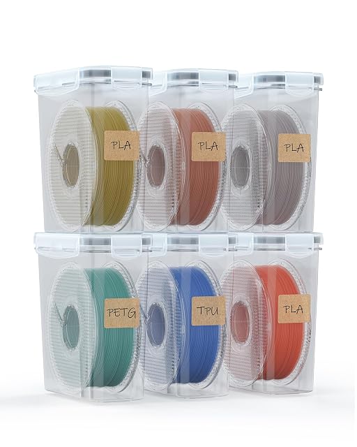 Sechs transparente Boxen in zwei Reihen gestapelt, jede mit einer Spule und einem Kraftpapieretikett PLA, PETG oder TPU